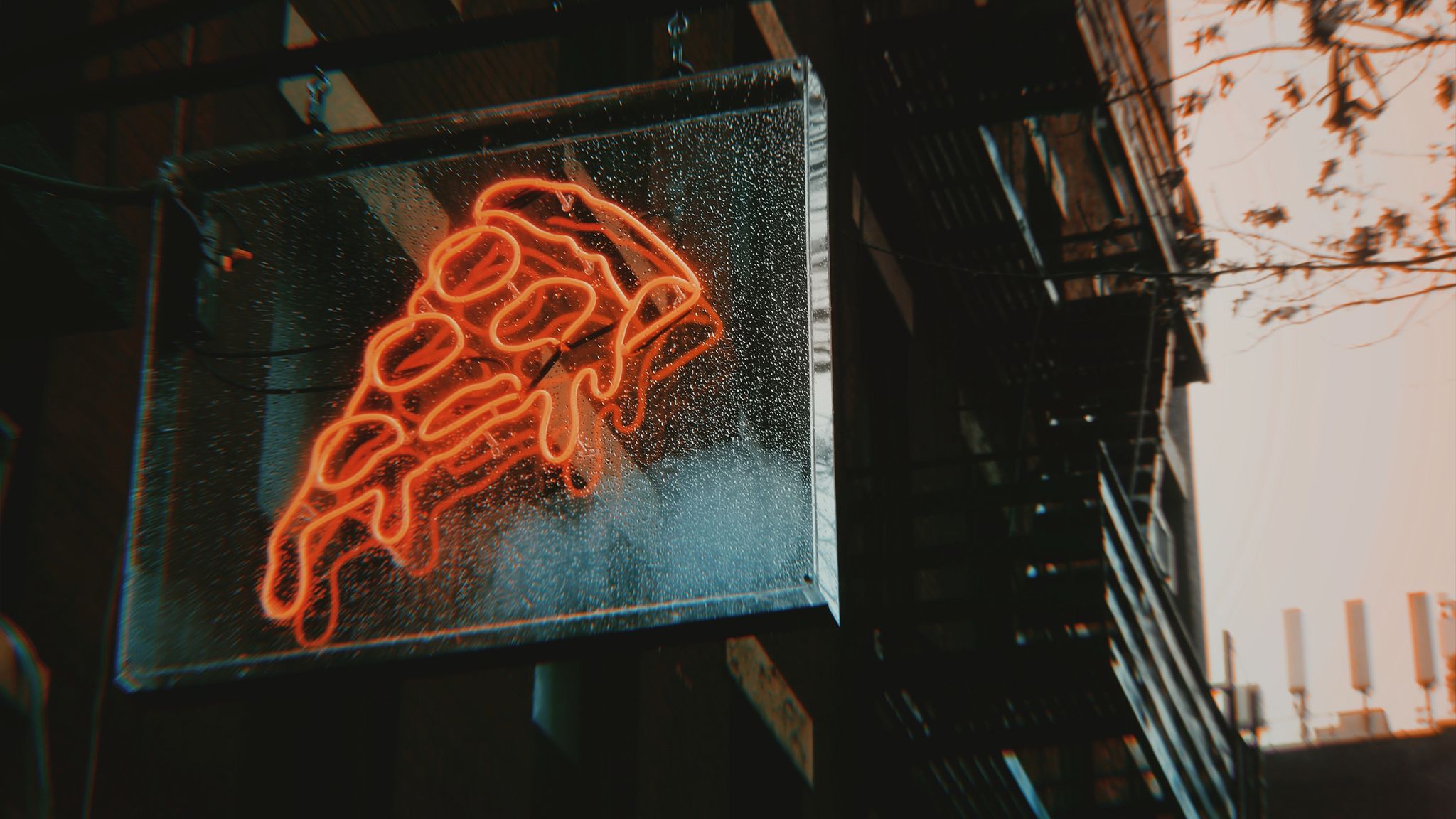 Neon sign of a pizza over a city's view